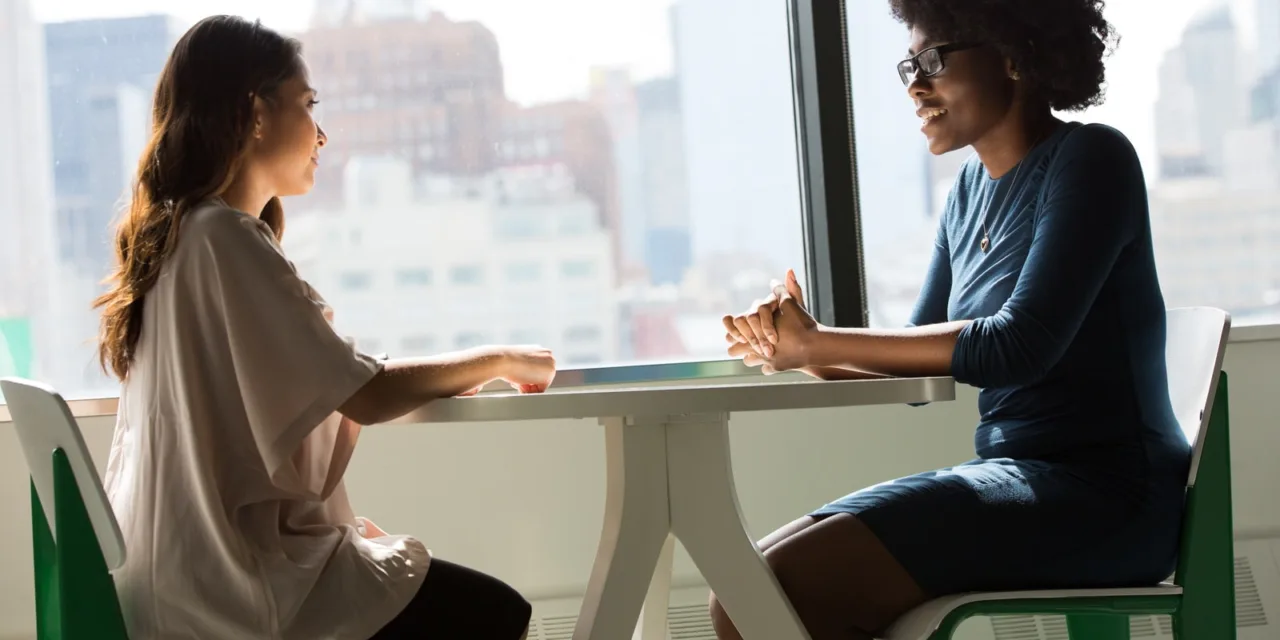 two women sitting beside table and talking